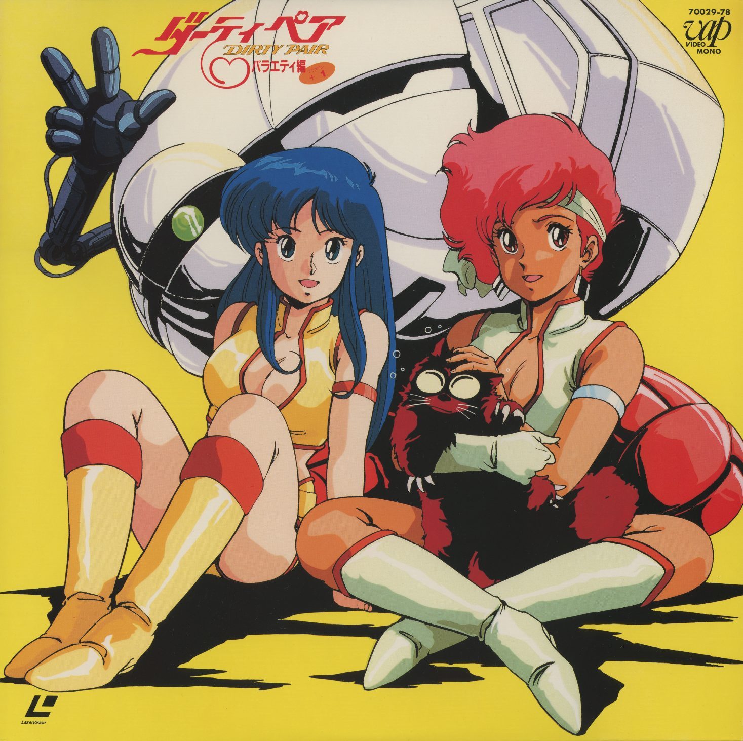 バラエティ編 +1 (Variety Edition) — VAP 70029-78. Kei and Yuri in red combat suits, seated, with the franchise cat Mughi (or its equivalent) in Kei's arms. A gloved mechanical hand reaches in from the top left. Yellow background. The idol register.