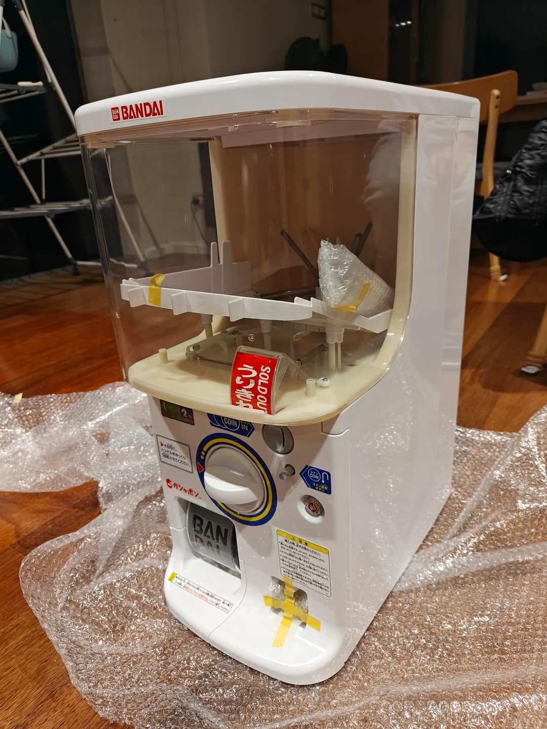 First unboxing — bubble wrap, yellow shipping tape, the SOLD OUT sign still in the capsule window. Bandai Capsule Station, fully mechanical, ready to load