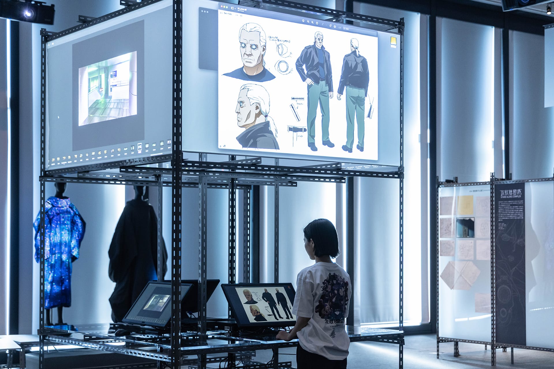 Digital archive terminals displaying character designs and production notes — four computer stations provide access to additional materials not physically exhibited, with ANREALAGE's thermochromic camouflage wearables visible in background