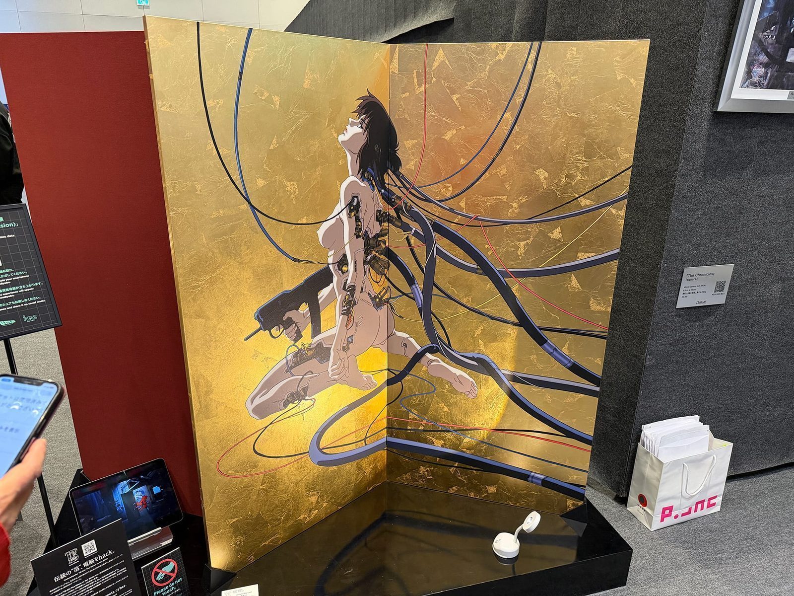 Techno Byobu — traditional gold-leaf folding screen with Major Kusanagi illustration, AR-enabled to overlay animated elements when scanned. Traditional craft meets franchise iconography.