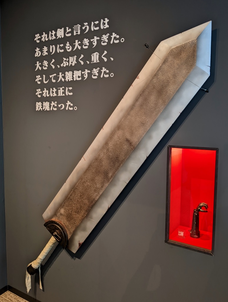 The Dragon Slayer and Behelit &mdash; Guts' oversized sword mounted on the wall beside the crimson egg, with the manga's most quoted description: &lsquo;It was too big to be called a sword&rsquo;