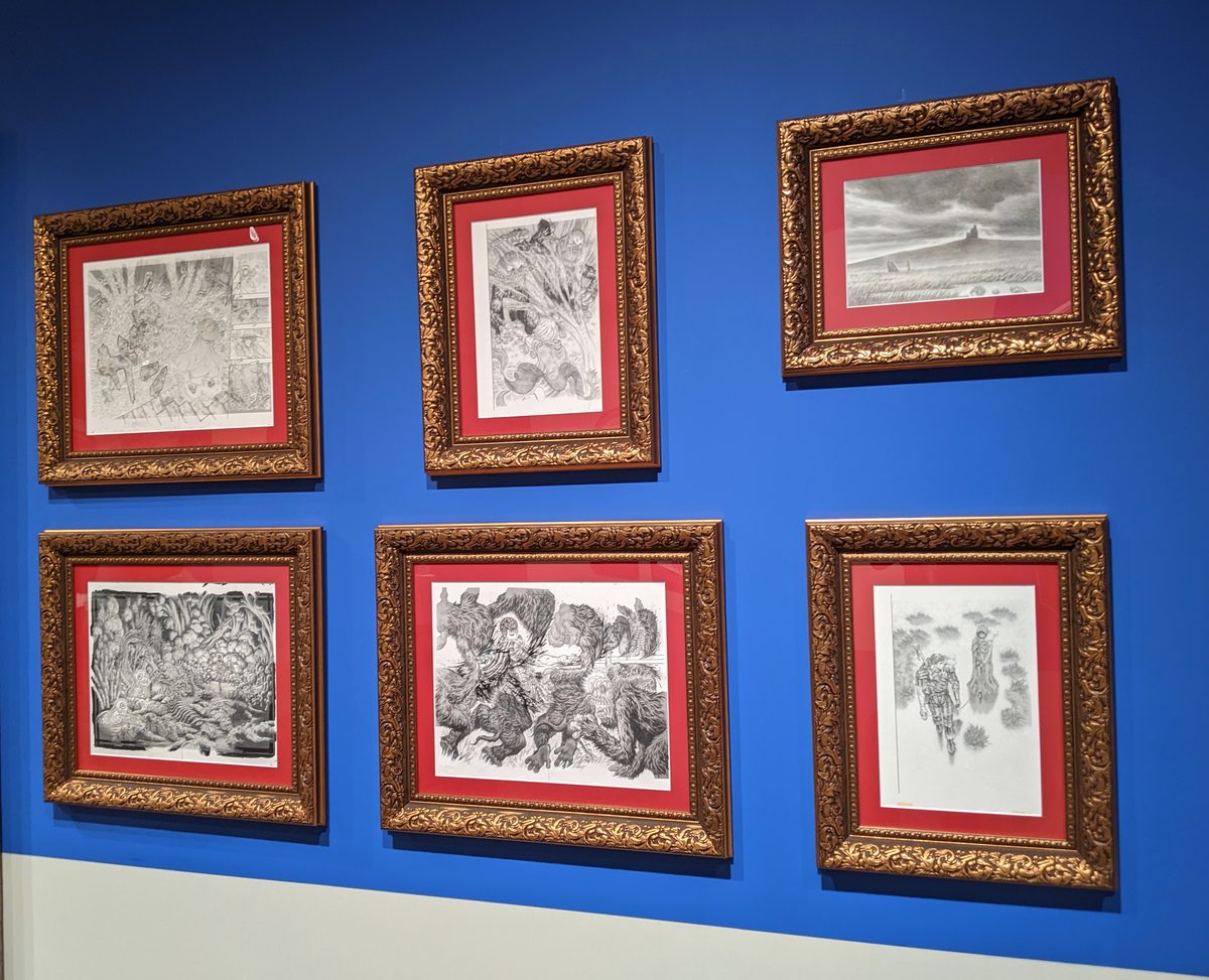 Original manuscripts in ornate gold frames &mdash; six of 300+ pages displayed at exhibition scale, Miura's obsessive hatching visible as physical labor rendered in ink
