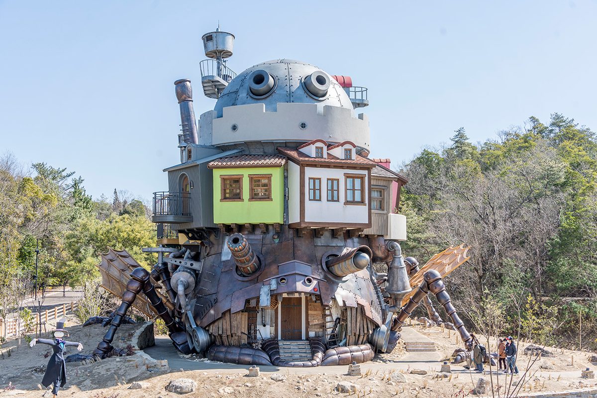 The castle's full height &mdash; dome, chimney stacks, green and pink upper buildings, copper mechanical legs and wing structure, visitors at the base providing scale