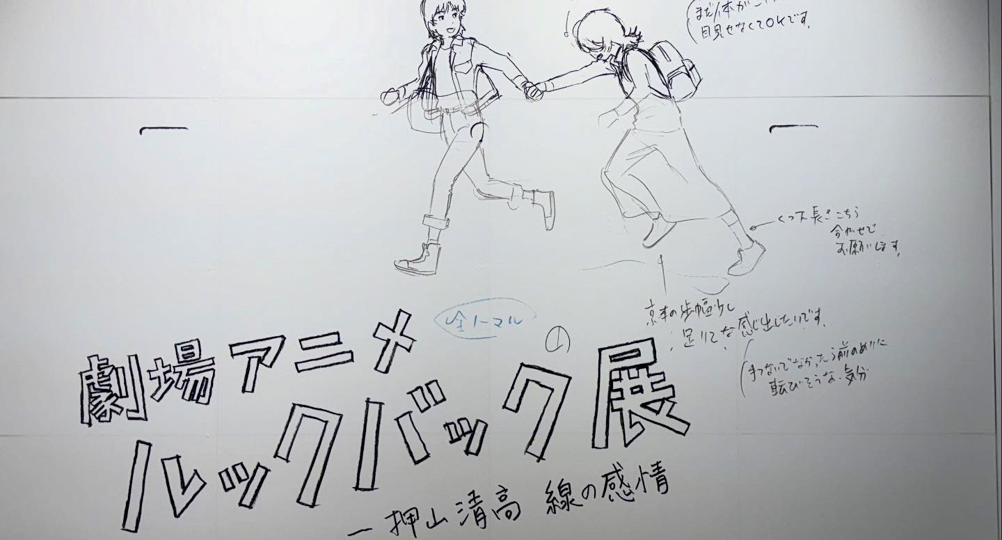 Oshiyama's wall drawing at the venue entrance — Fujino and Kyomoto running, with handwritten animation notes: 京本の歩幅ちいさく、足にそんな感じ出ています (Kyomoto's stride is small, that feeling shows in her feet)