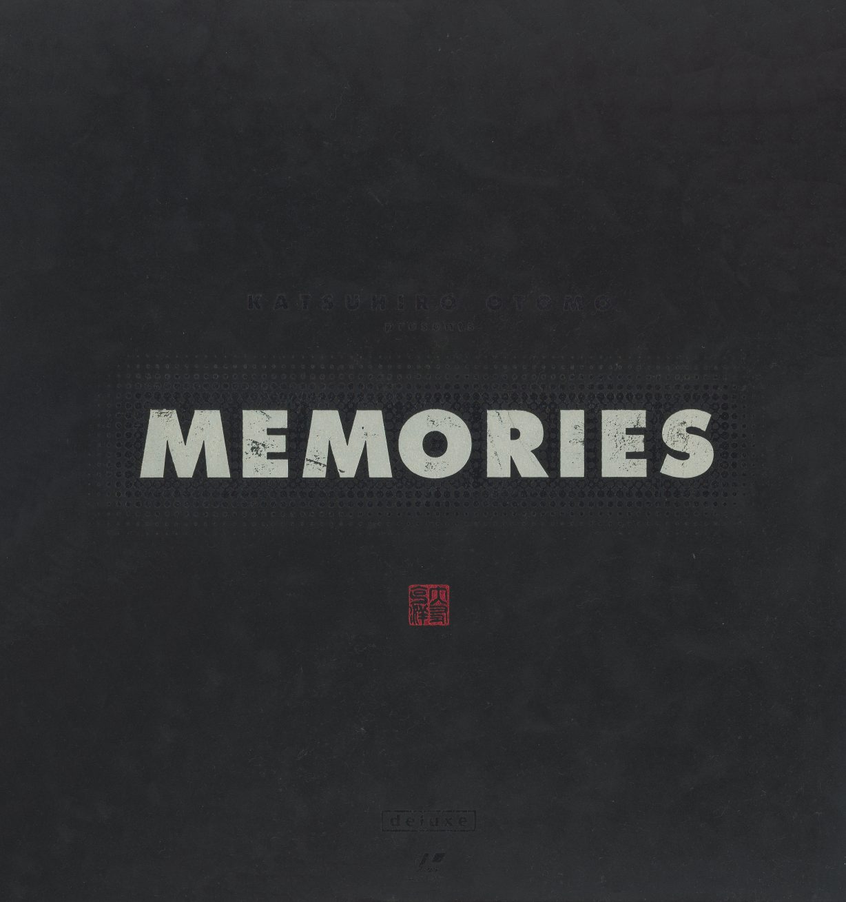 Outer box exterior — "MEMORIES" in silver-white letterforms on dark charcoal field. Red hanko stamp below. No episode titles, no synopsis, no key art. The entire exterior reduces to a title and a seal.