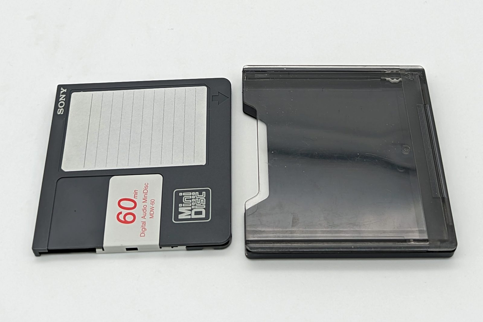 Sony MDW-60 MiniDisc and case — the cartridge shell borrowed from 3.5-inch floppy logic. Physical protection mattered more than capacity