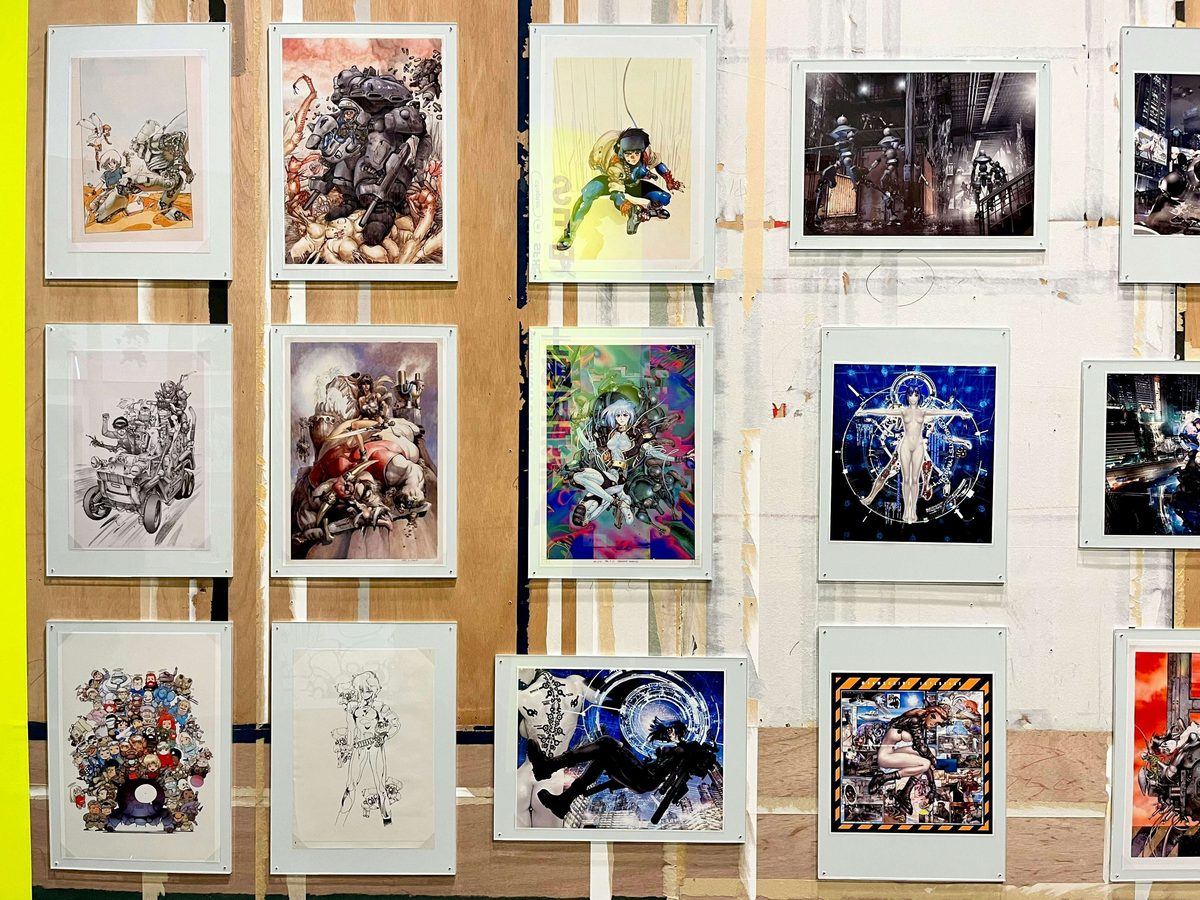 Gallery wall &mdash; framed color illustrations spanning Ghost in the Shell, Appleseed, and Shirow's full catalog, displayed across the exhibition's chronological sections