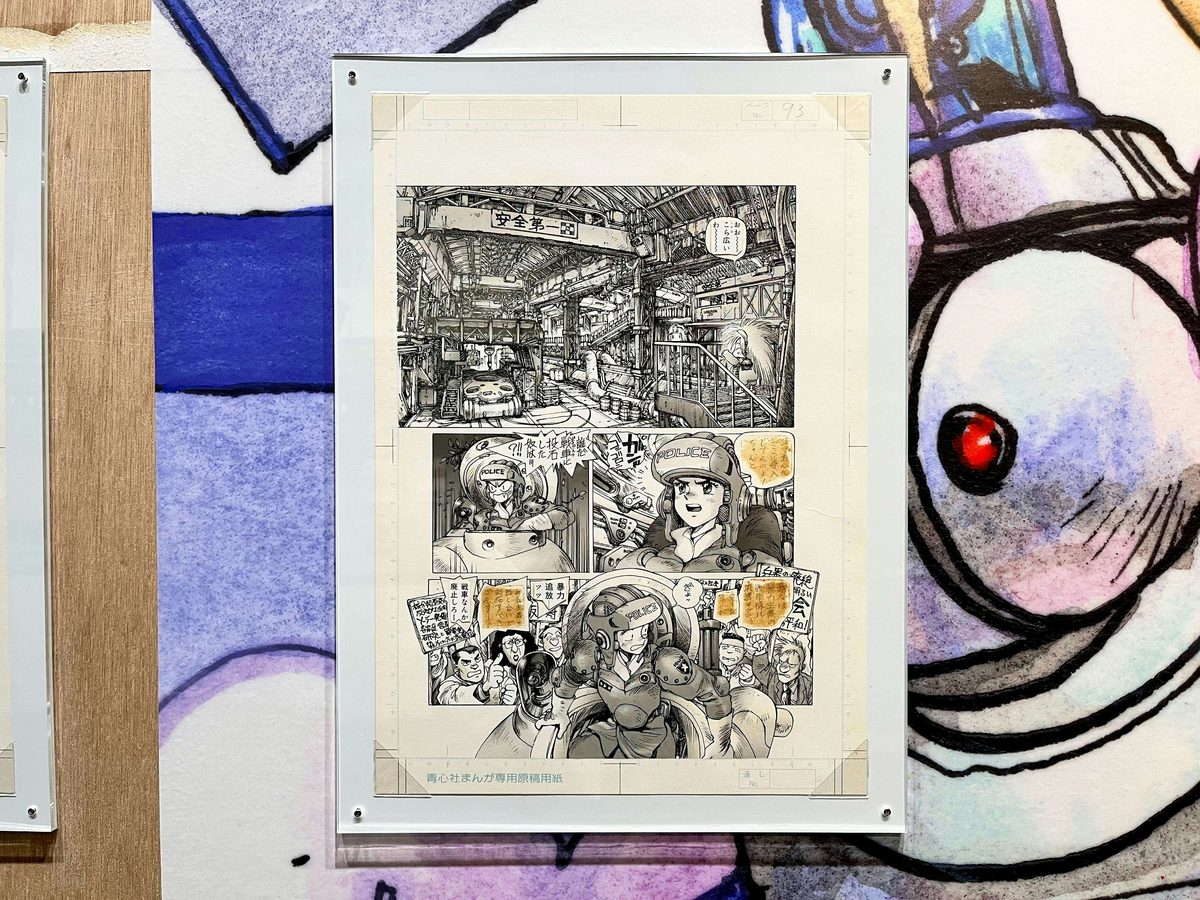 Original manga page displayed at exhibition scale &mdash; Shirow's ink density and panel architecture visible in a way the tankoubon format cannot reproduce