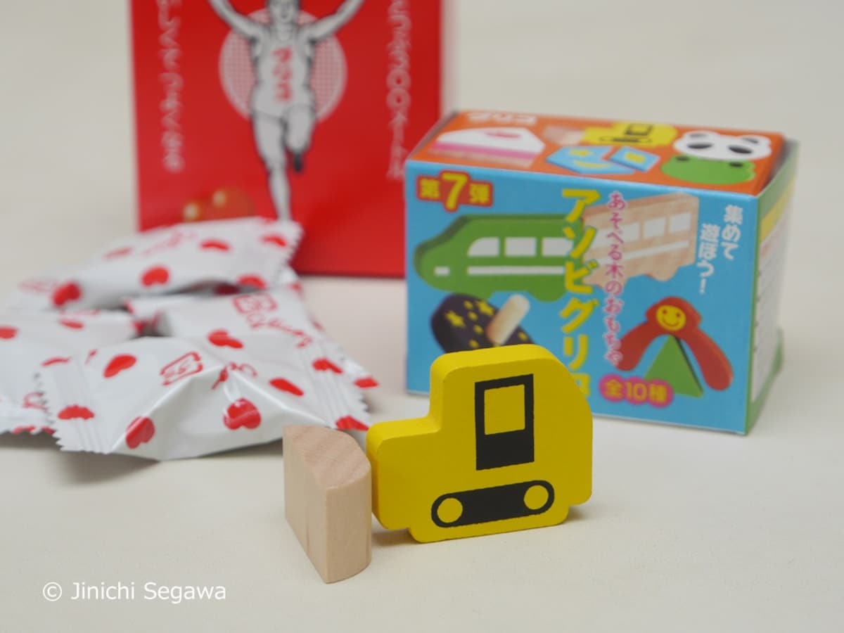 Close-up of Glico's wooden omake toy alongside heart-shaped caramels — the 1927 formula unchanged