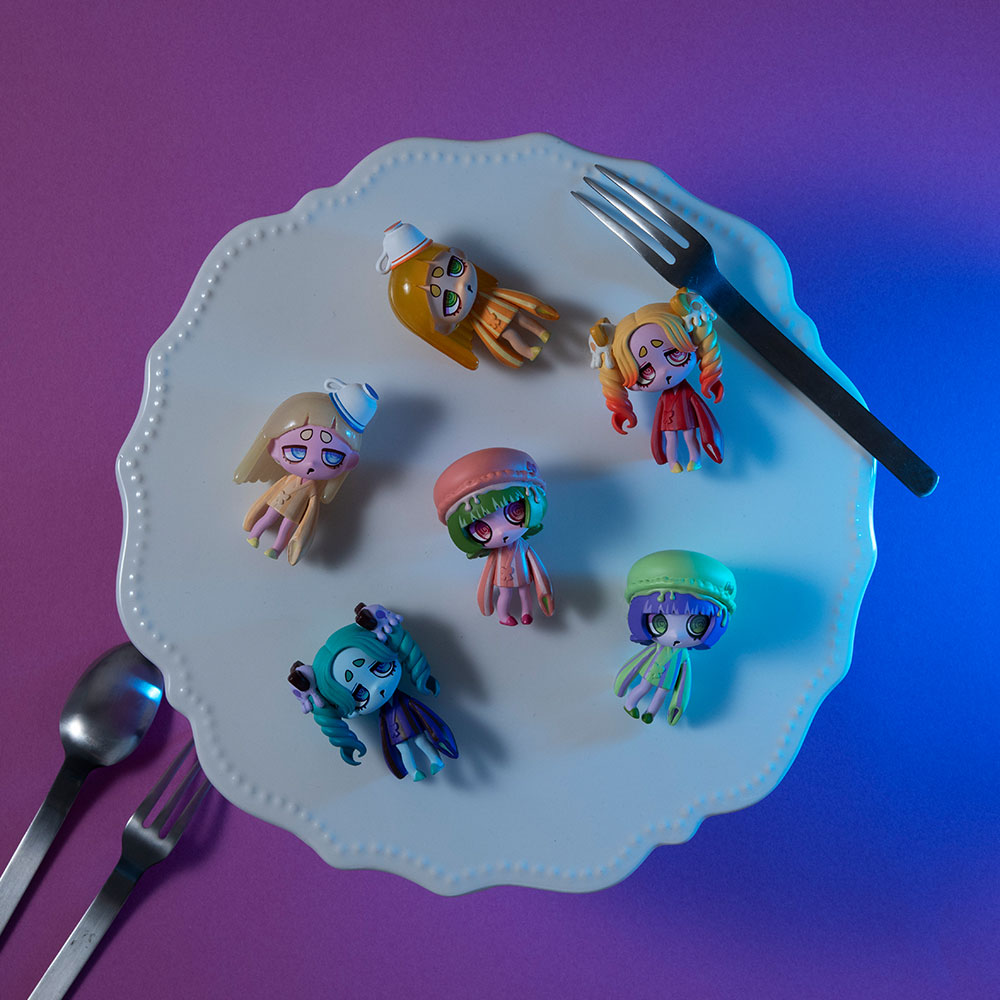 Tea Break series on a plate with tiny fork and spoon. Macarons, Scones, Lemon Tea. The staging suggests a meal interrupted.