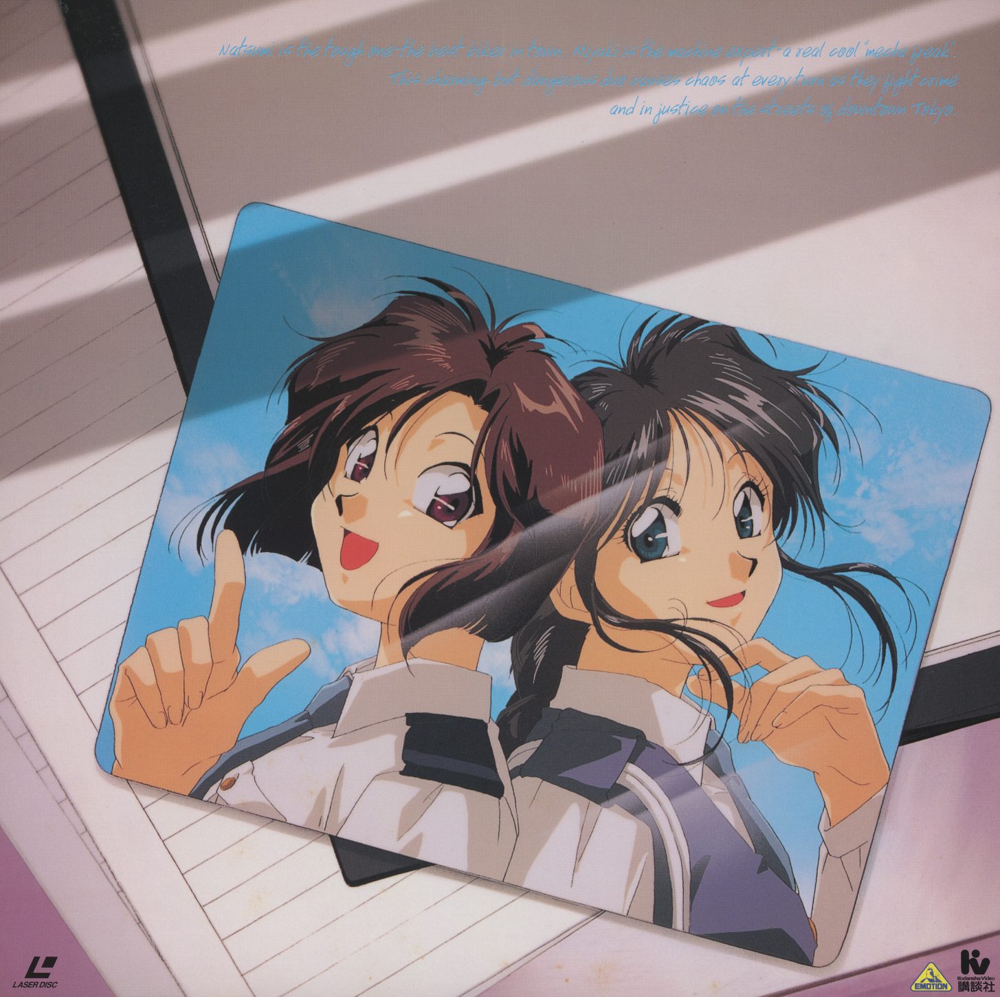 File 4 gatefold interior — Natsumi and Miyuki rendered as a Polaroid photograph lying on lined notebook paper, both pointing toward the viewer. Not a Fujishima painting but a photograph of a photograph — the final volume frames the characters as documentation rather than illustration.
